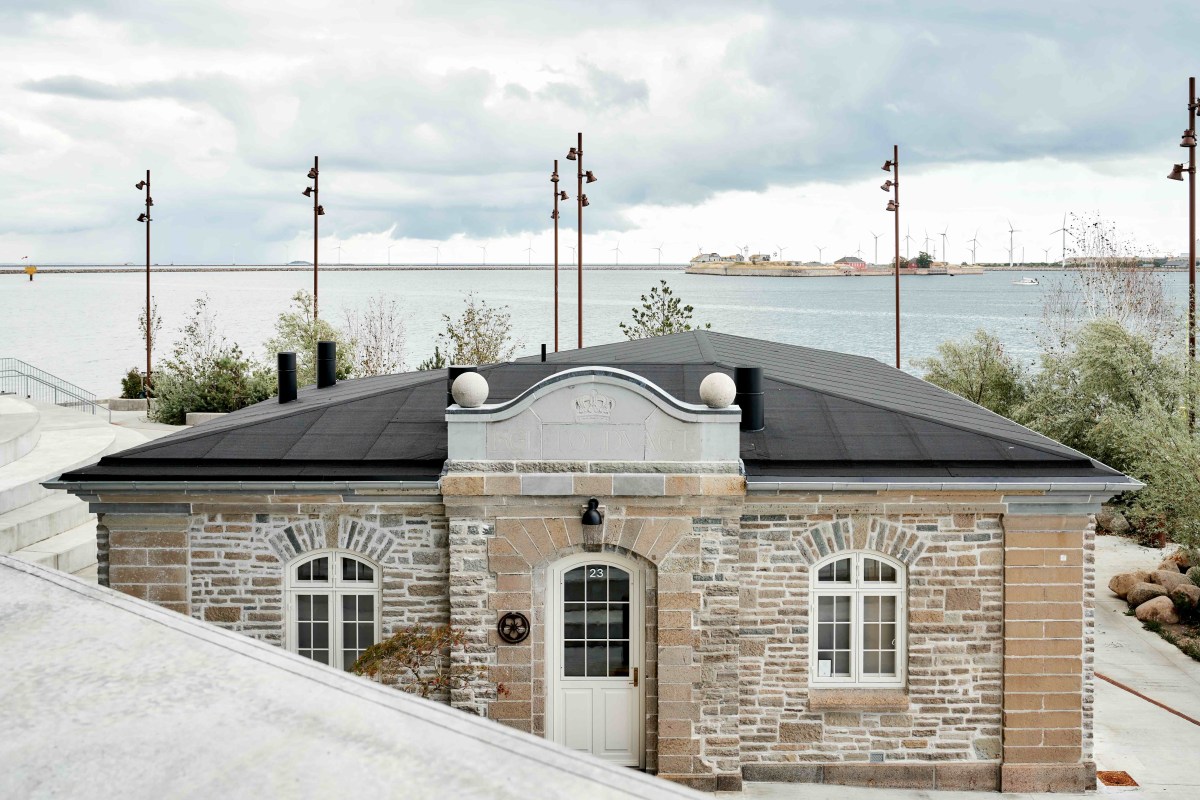 Stone exterior of Sushi Anaba building with dark roof, waterfront view and wind turbines in background