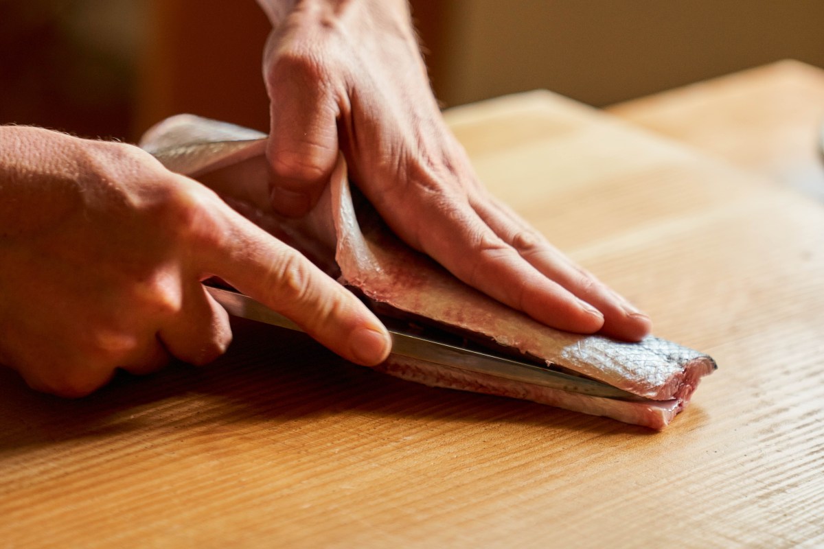 Close-up of hands filleting a fish with a knife on a wooden cutting board