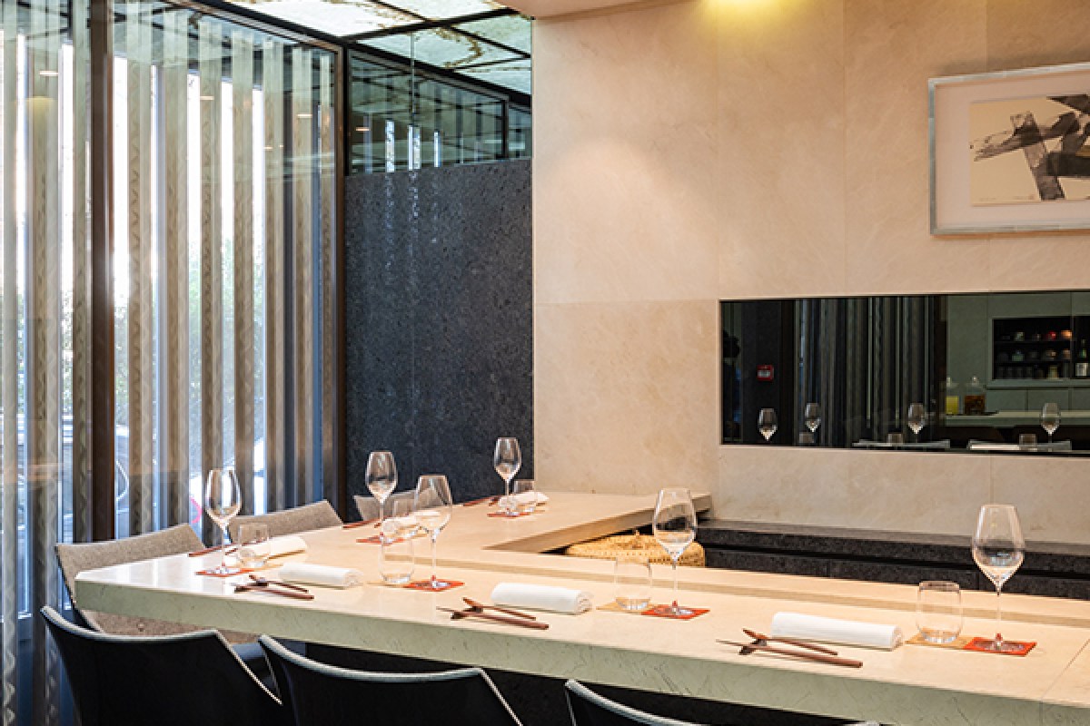 Restaurant dining counter with place settings, wine glasses, and view through slatted windows to street