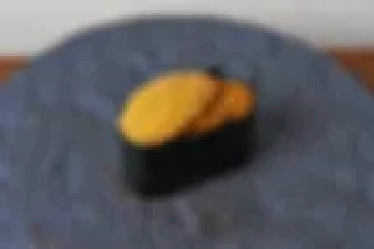 Close-up of a single piece of nigiri sushi with egg topping on a dark plate