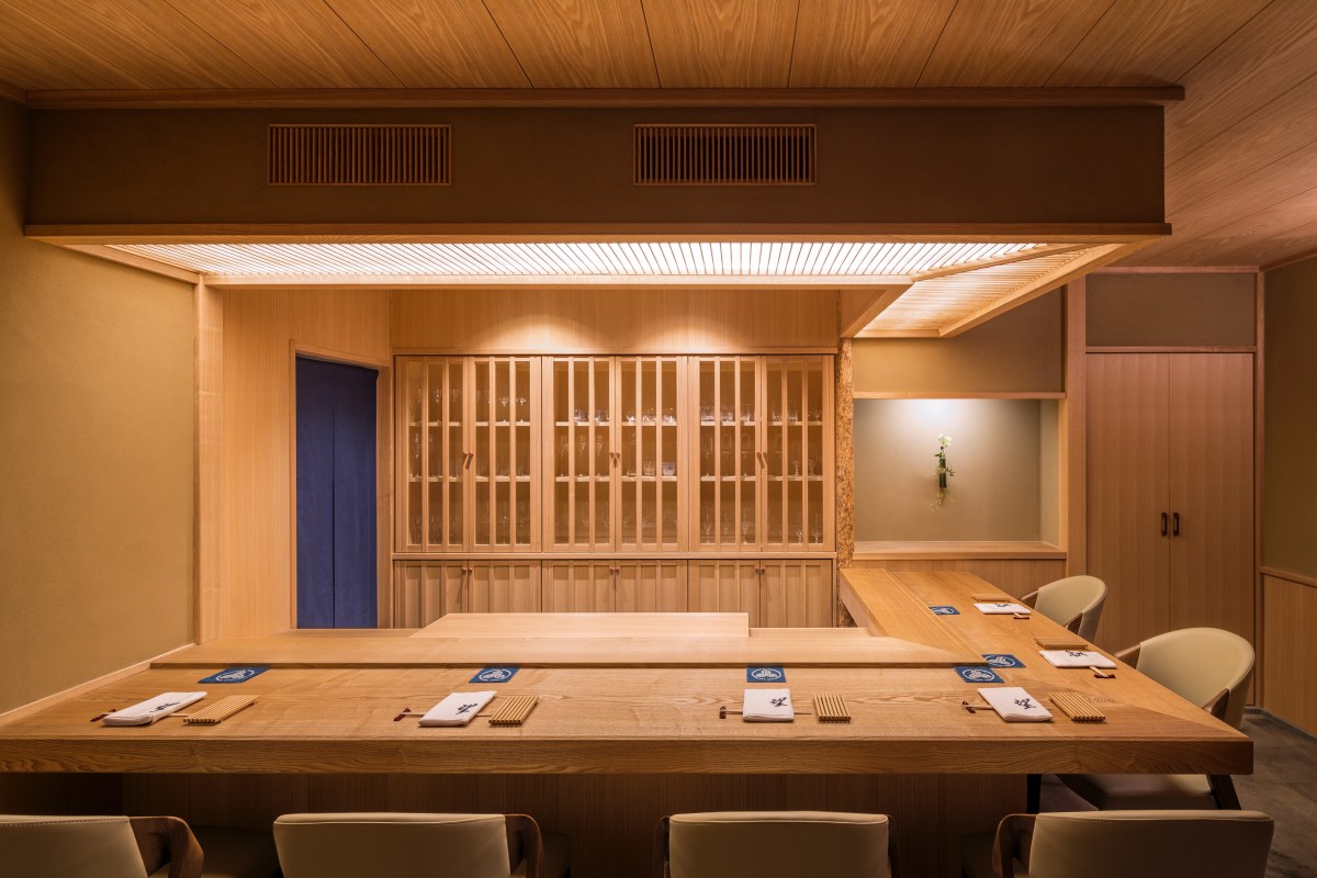 Wooden sushi bar with glass cabinets, place settings, and soft lighting in a traditional Japanese-style dining room