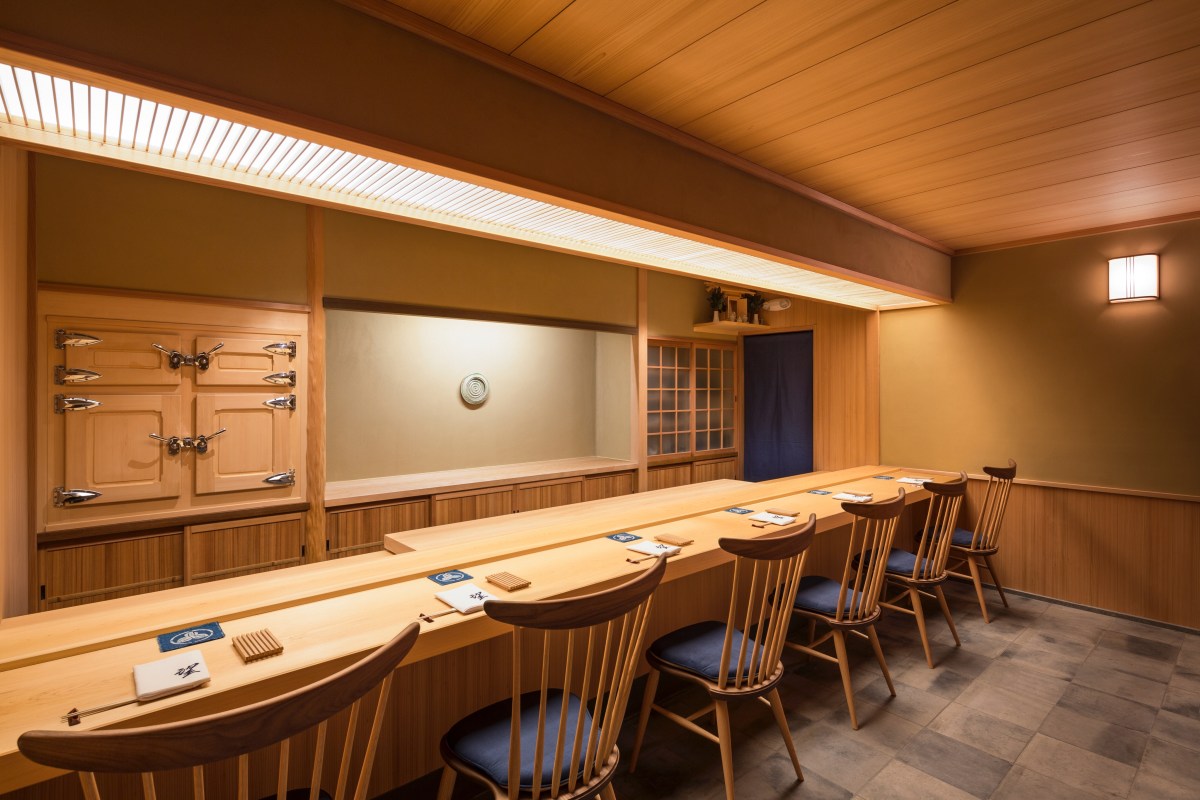 Wooden sushi counter with place settings, chairs, and traditional Japanese wall fixtures in a minimalist dining room