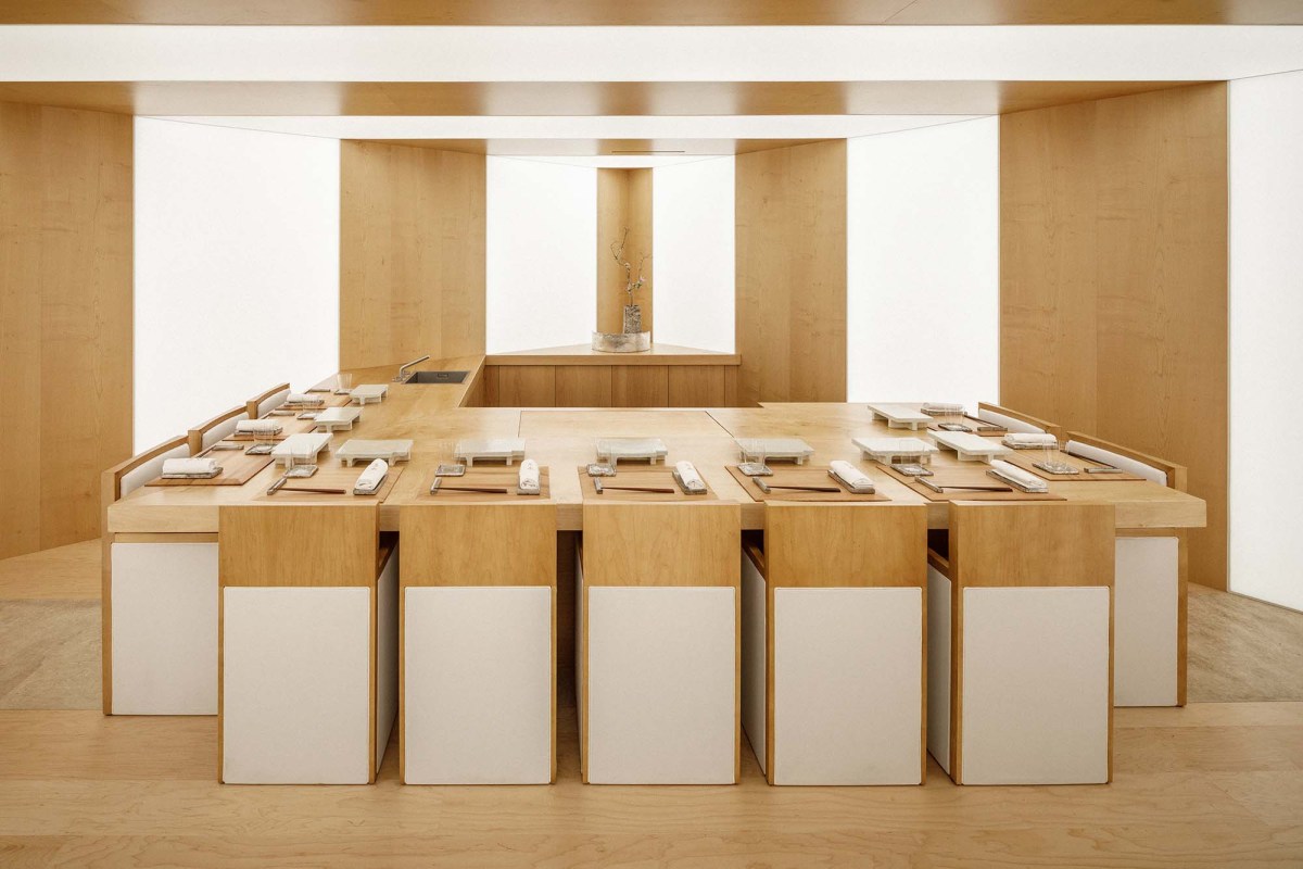 Minimalist wood-paneled sushi counter with white stools and place settings