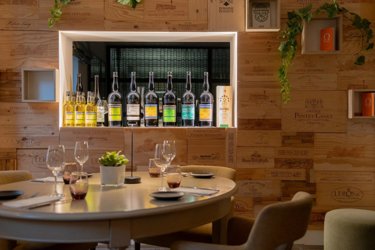 Dining table with wine glasses in front of a wall of wine crates and a lit bottle display