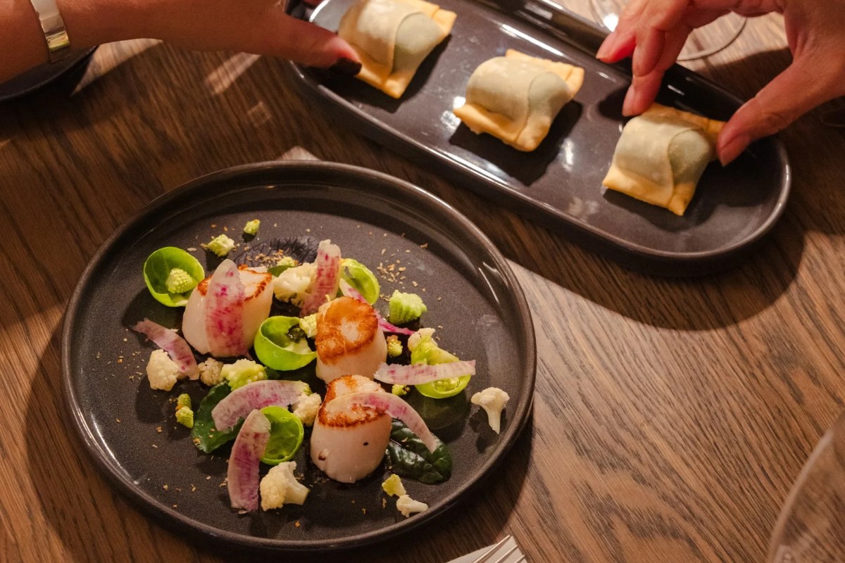 Plate of seared scallops with cauliflower and radish, plus a tray of dumplings on a wooden table