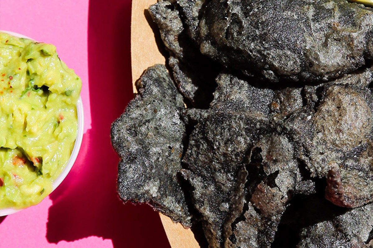 Blue corn tortilla chips served with a side of guacamole on a pink background