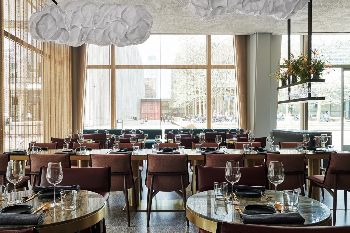 Restaurant dining room with cloud-like pendant lights, set tables and large windows overlooking plaza