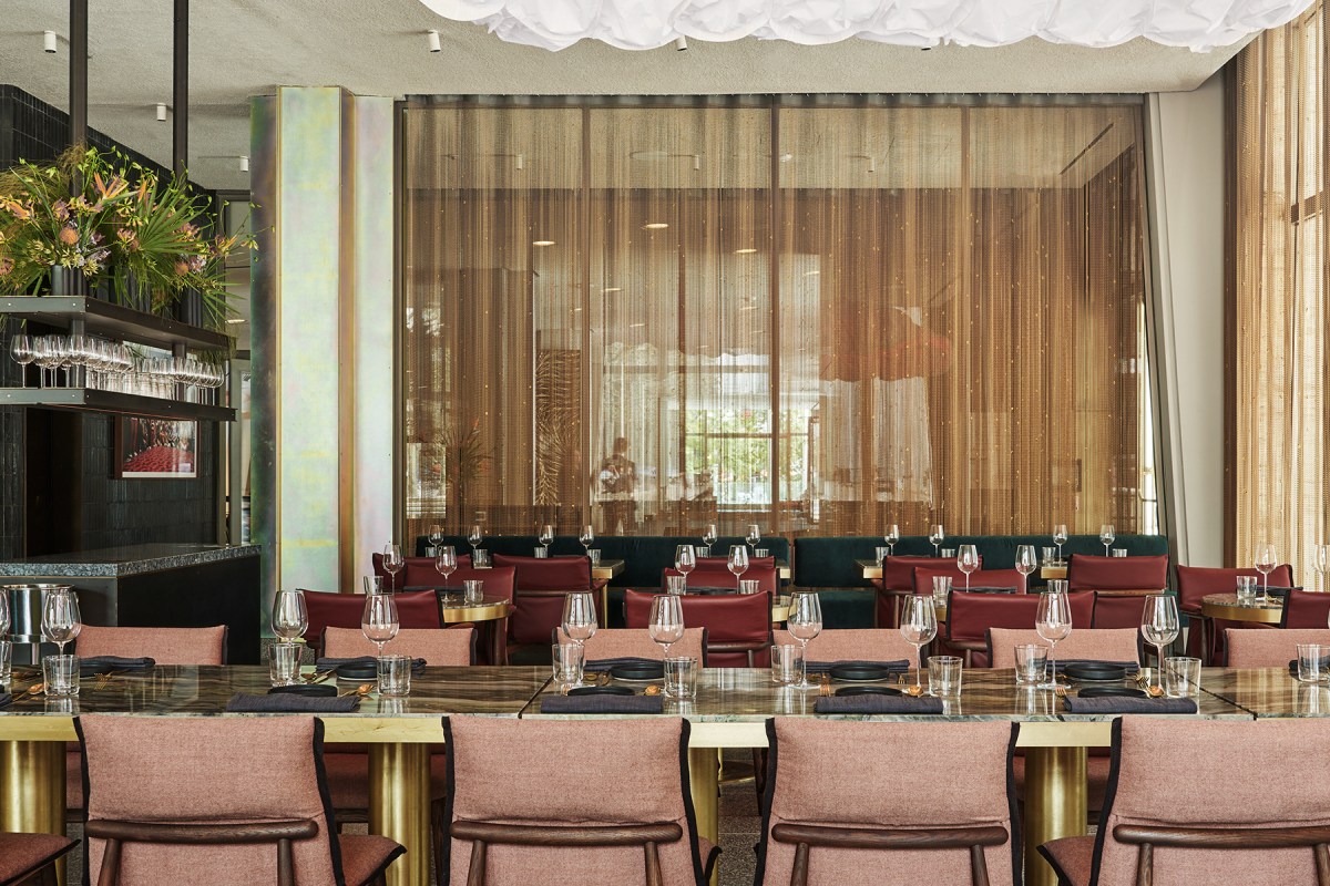Restaurant dining room with pink chairs, marble tables, bar and mesh curtain
