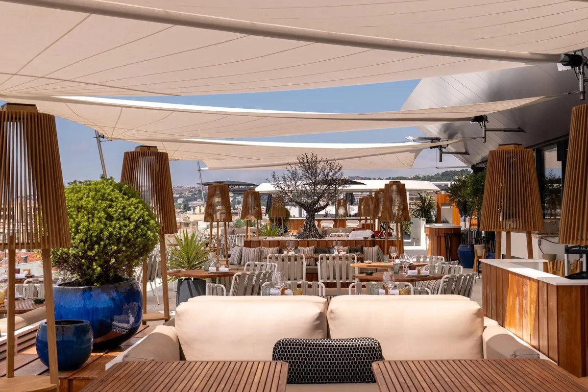 Taulissa's rooftop terrace on the sixth floor of Le Victoria in Nice, with tables set under white sail awnings, wooden lanterns and an olive tree
