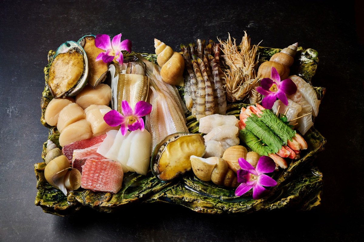 Elaborate sashimi platter with scallops, abalone, shrimp, and orchid garnish on a mossy green plate