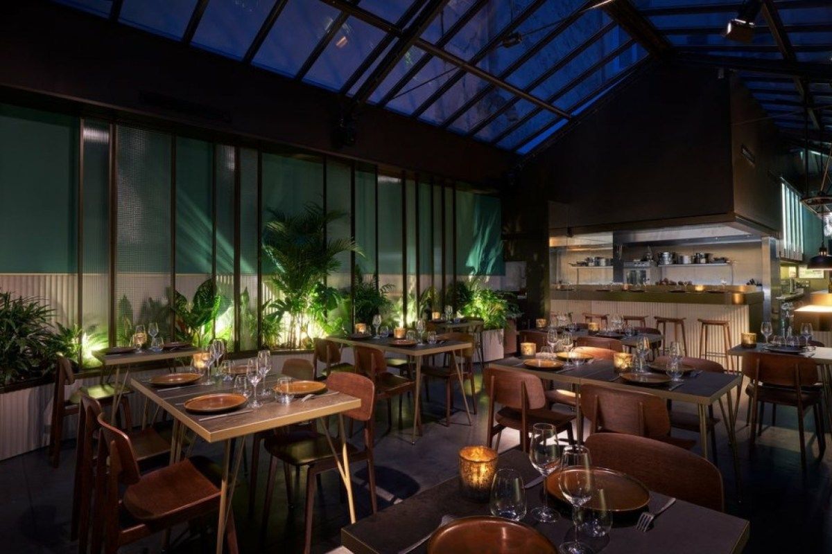 Terra dining room at dusk with glass roof, plants and open kitchen, tables set with candles