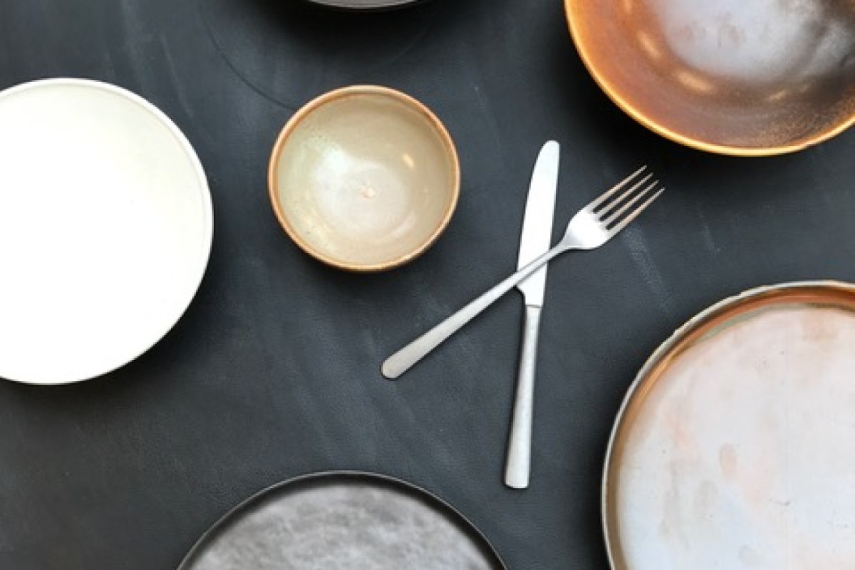 Flat lay of ceramic plates, bowl and crossed cutlery on dark table at Terra