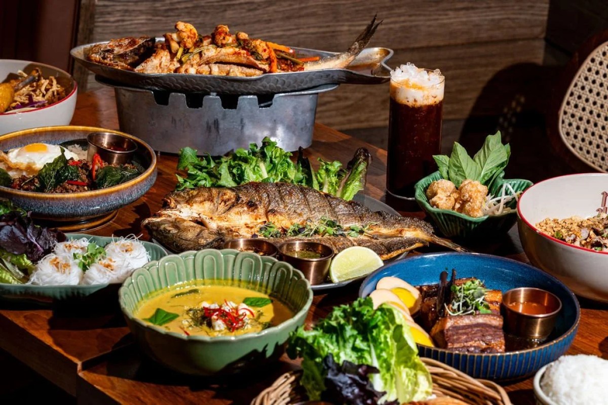 Spread of Thai dishes on a wooden table including whole grilled fish, green curry, and rice