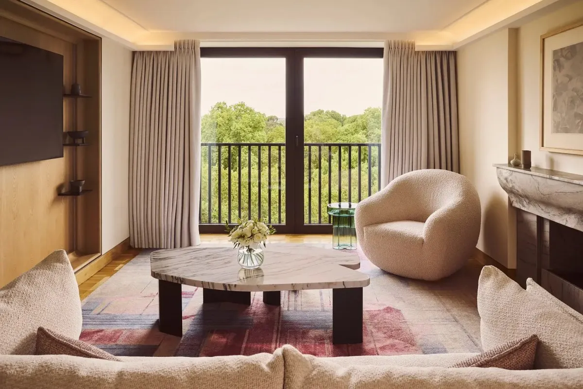 Hotel suite living room with cream sofa, marble coffee table, armchair and balcony overlooking green trees
