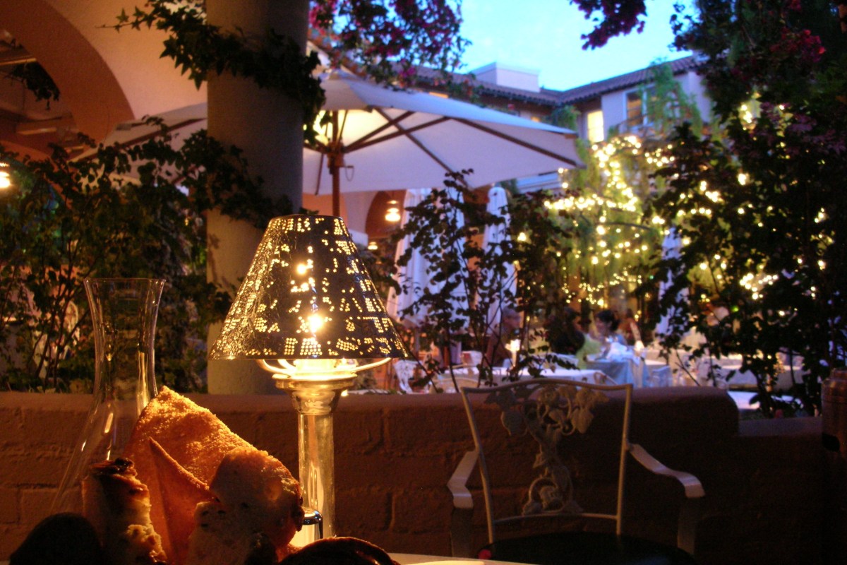 Evening view of Polo Lounge terrace with string lights, umbrellas, and garden greenery