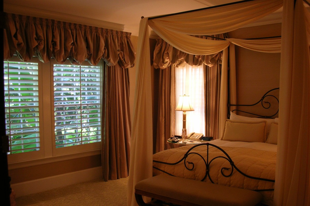 Elegant guest room with canopy bed draped in cream fabric and shuttered window