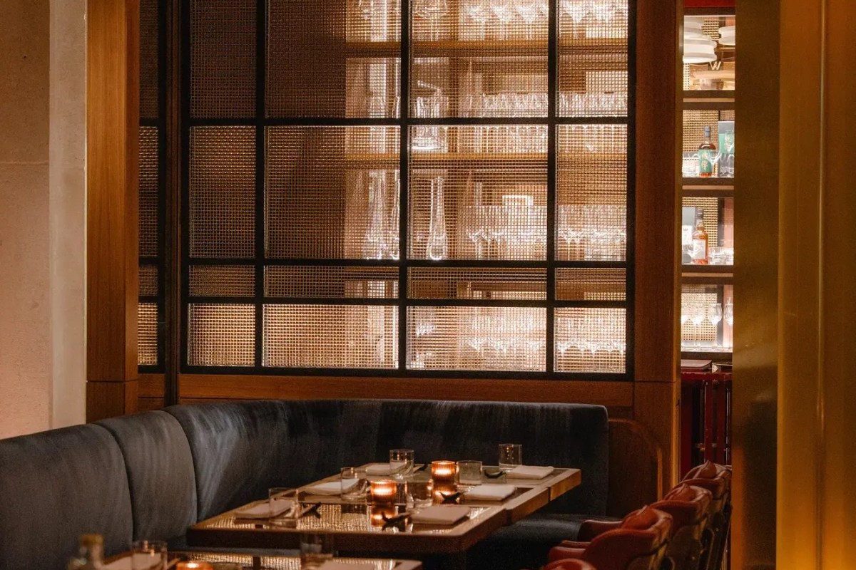 Intimate hotel restaurant booth with velvet seating, candlelit table and a glass-walled wine display behind