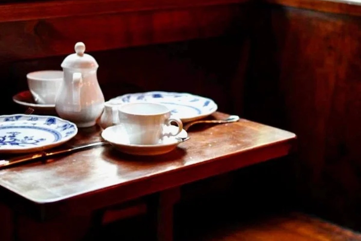 Close-up of a wooden table set with blue-and-white patterned china, a teapot, and silverware in a dimly lit dining room.