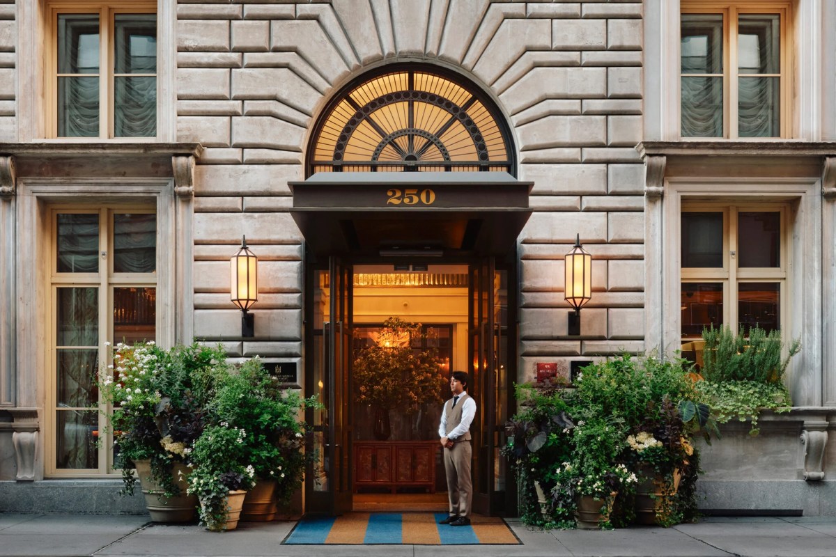 Hotel entrance at dusk with arched doorway, lanterns, greenery, and a doorman at the door