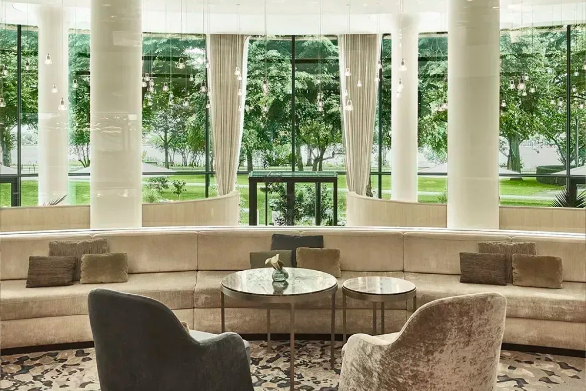 Hotel lounge with curved beige sofa, pillars, and floor-to-ceiling windows overlooking a green garden