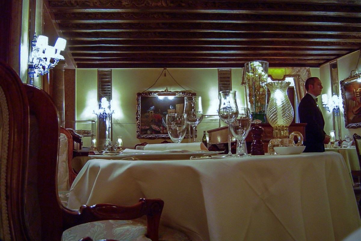 Elegant hotel dining room with set table, chandeliers and a waiter in the background