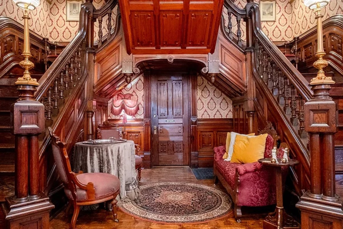 Grand wood-paneled foyer with twin staircases, antique furniture, and ornate rug
