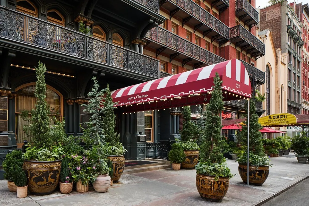 Daytime view of Hotel Chelsea entrance with red-and-white striped awning, potted trees, and wrought-iron balconies