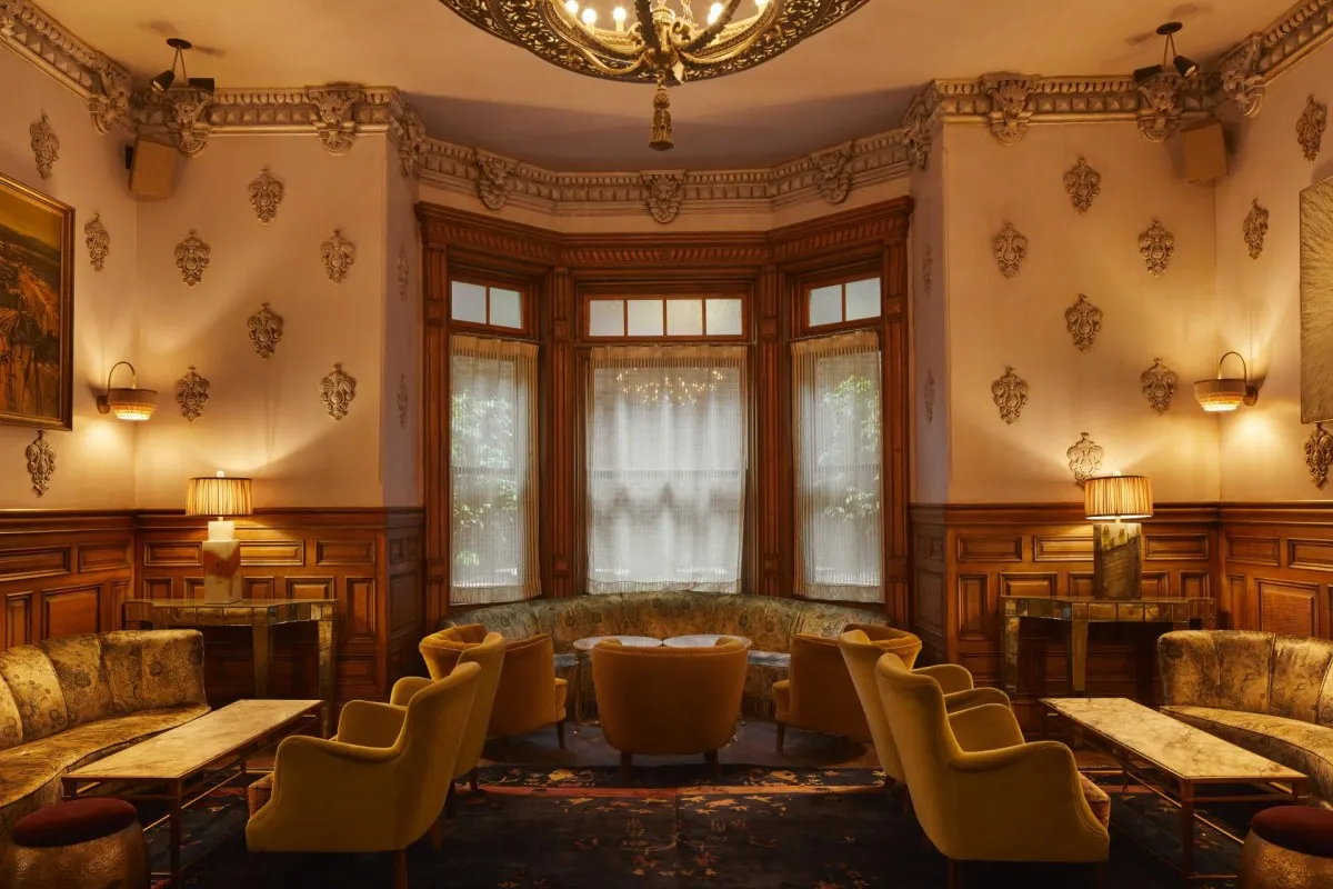 Elegant hotel lounge with ornate wood paneling, velvet armchairs, a chandelier, and a bay window