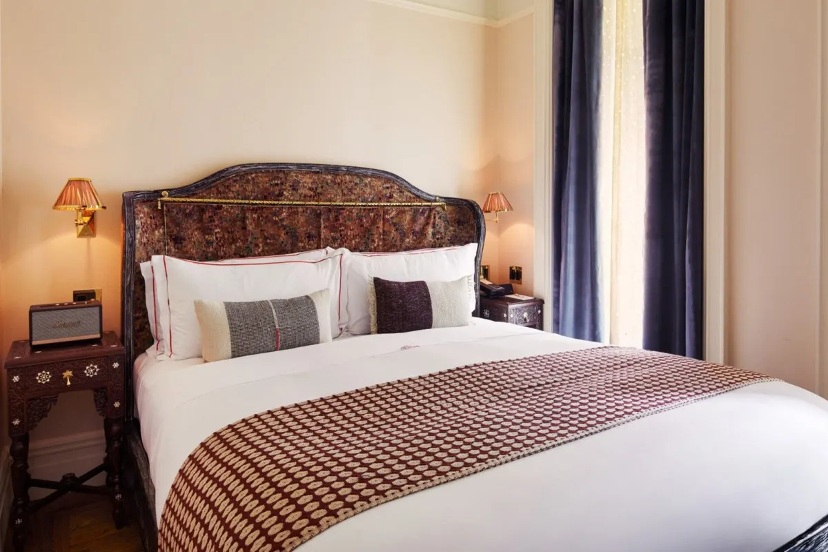 Hotel guest room with a patterned headboard, white bedding, dark velvet curtains, and bedside lamps