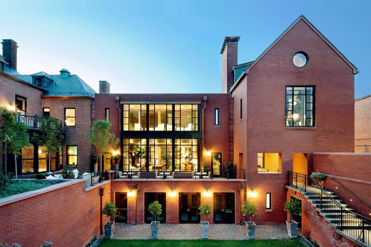 Twilight view of The Ivy Hotel's brick exterior with illuminated windows, courtyard patio, and manicured topiaries