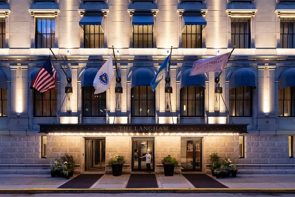 Evening view of The Langham Boston's illuminated stone façade with flags, awnings, and entrance