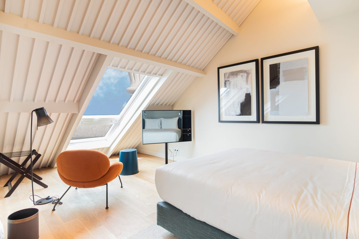 Hotel attic guest room with sloped skylight ceiling, white bed, orange armchair and artwork