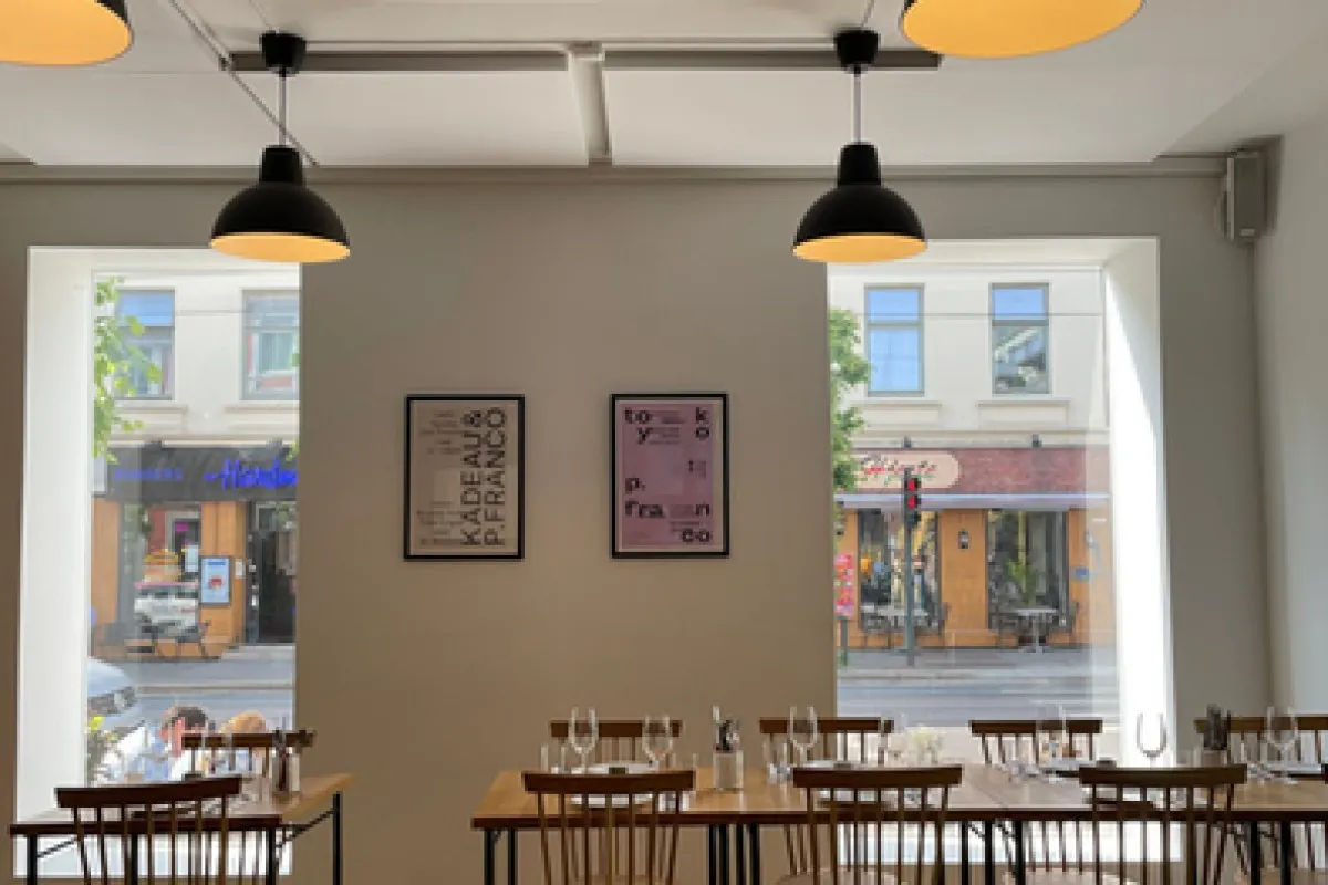 Bright dining room interior with pendant lights, framed posters, and large windows showing the street outside