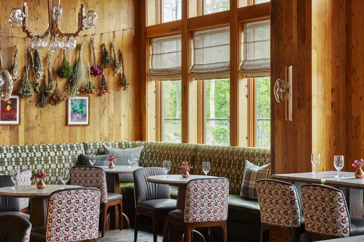 Rustic lodge restaurant/bar with wood walls, hanging herb bundles, patterned chairs and large windows