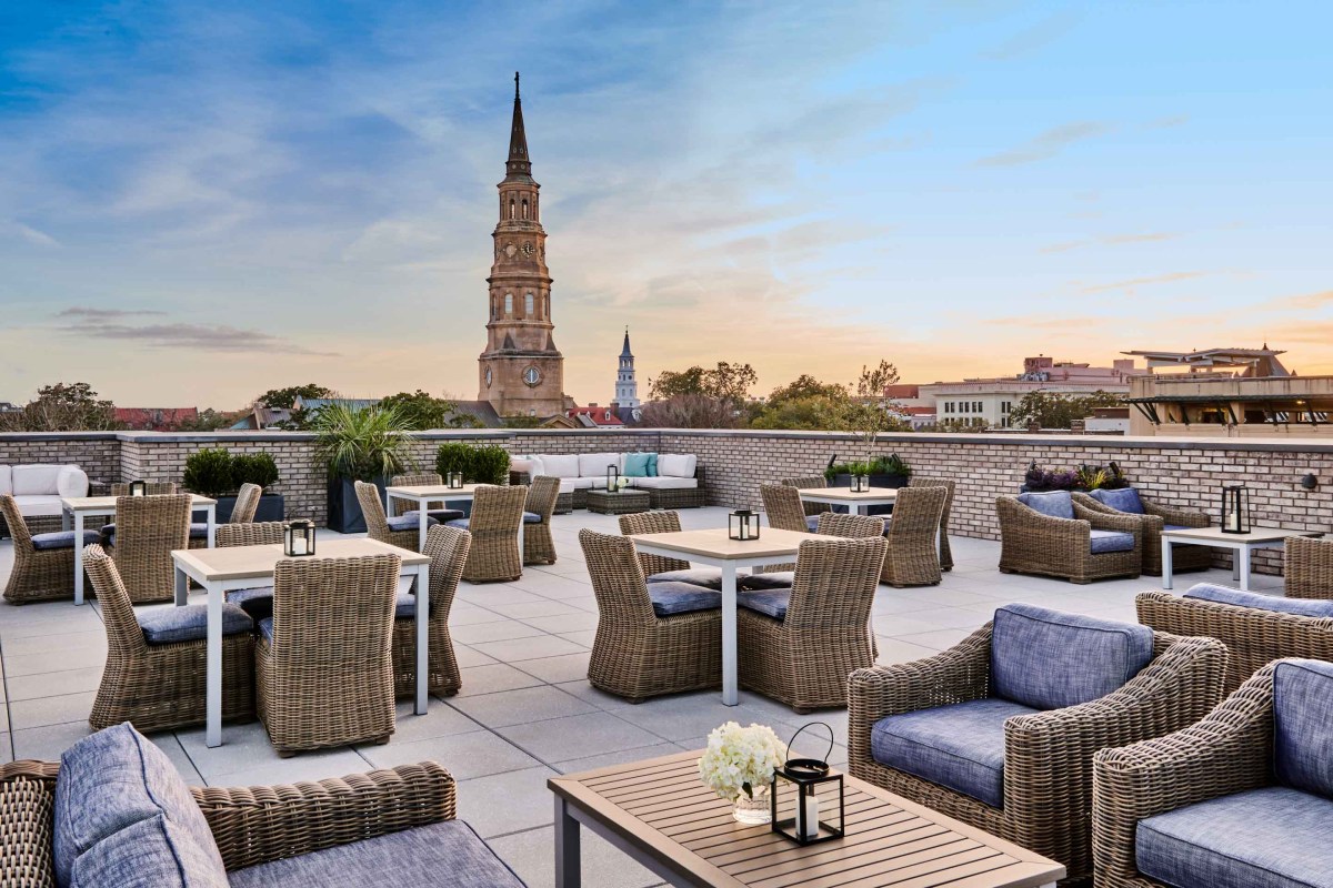 Rooftop terrace with wicker furniture overlooking Charleston church steeples at sunset