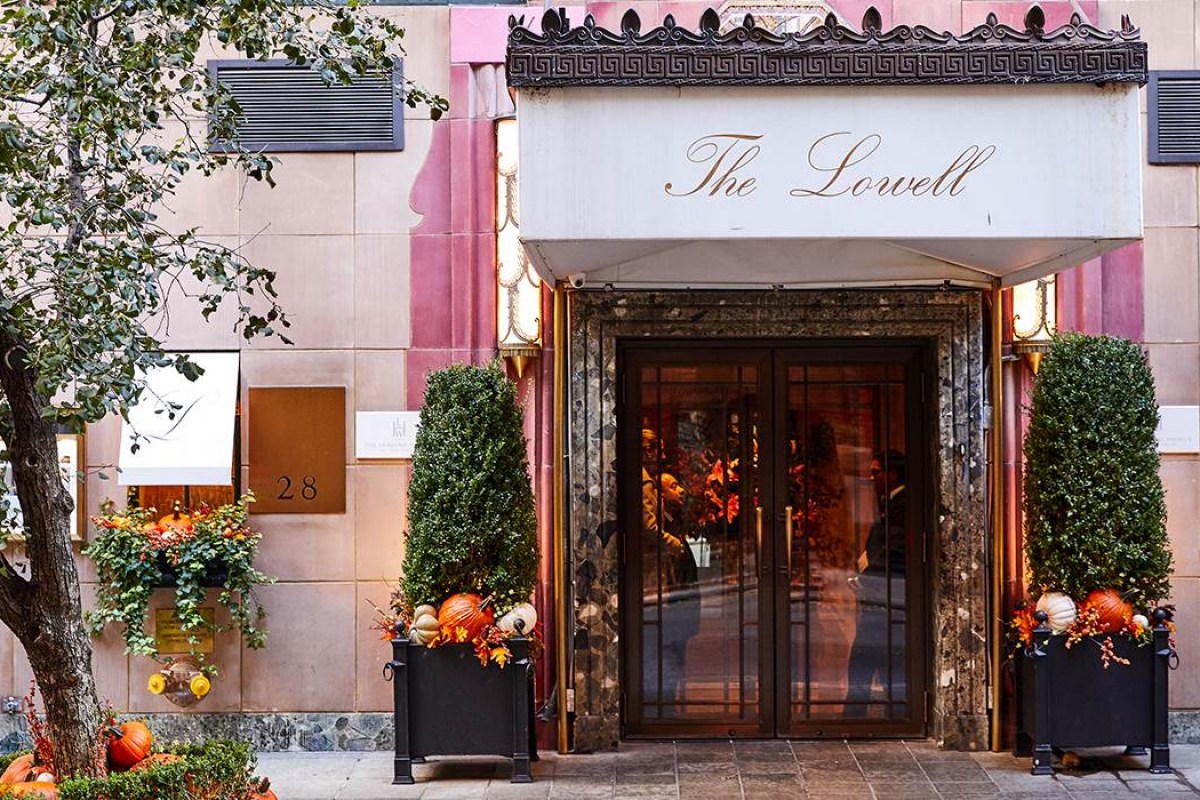 Entrance façade of The Lowell hotel with awning reading 'The Lowell' and topiary planters flanking the door