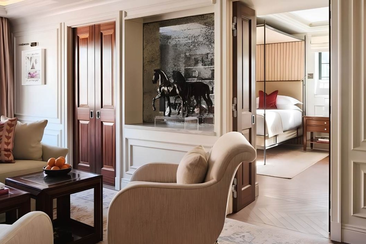 Hotel suite with sitting area and horse sculpture artwork opening into a bedroom with canopy bed