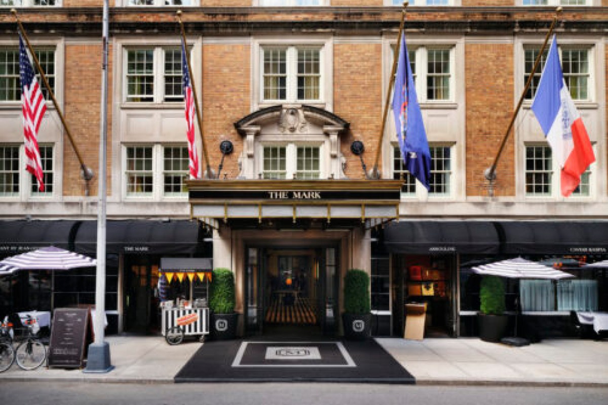 Street-level facade of The Mark Hotel with awning, four flags, outdoor umbrellas and brick building