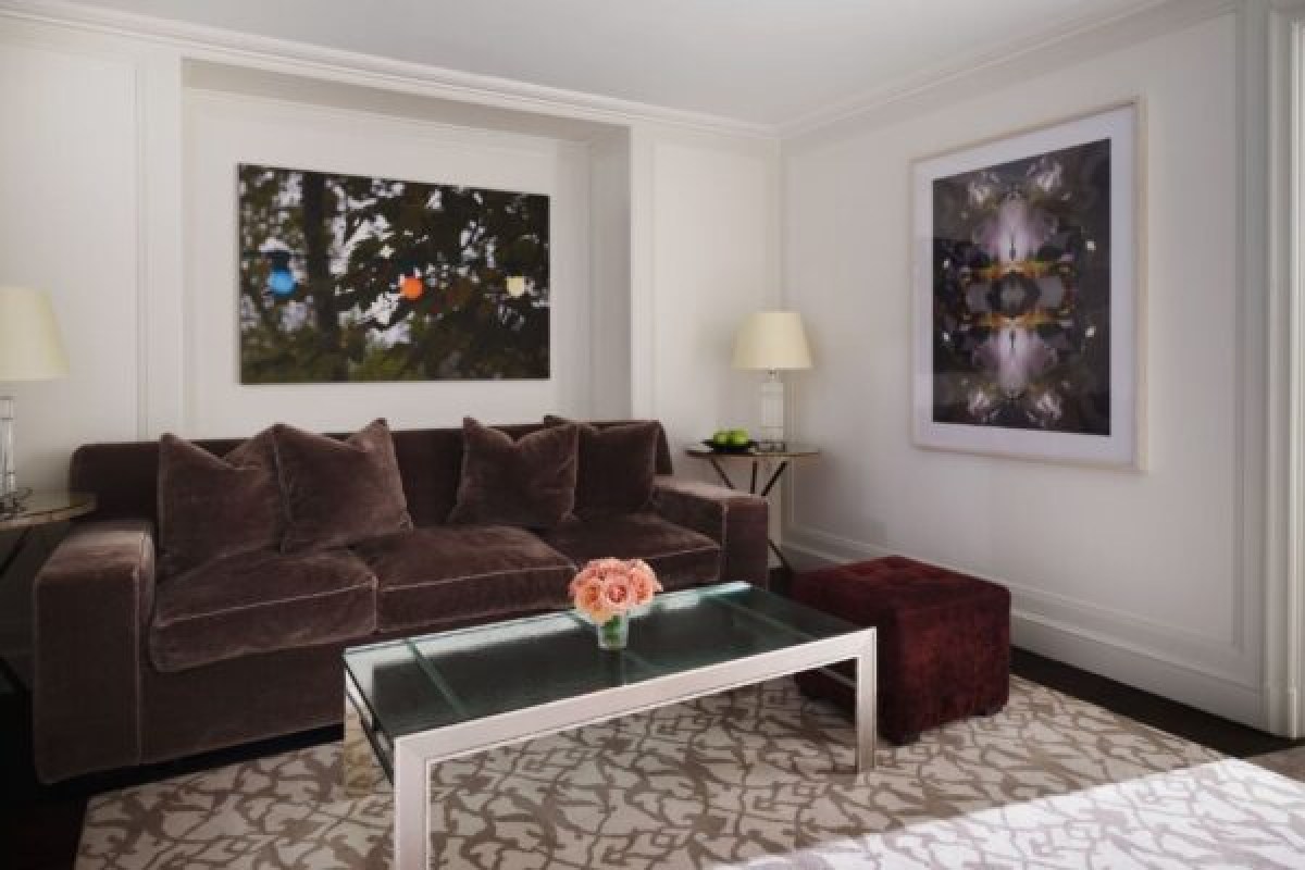 Hotel suite living area with brown velvet sofa, glass coffee table, and modern art on cream walls.
