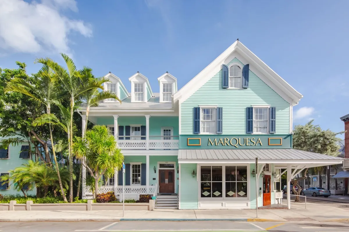 Daytime view of The Marquesa Hotel's mint-green Victorian facade with palm trees and the Marquesa sign above the entrance