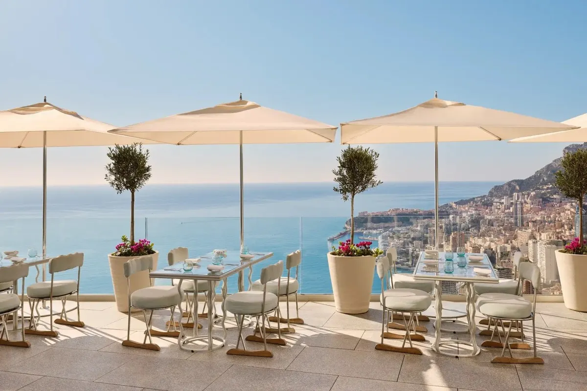 Hotel terrace restaurant with white umbrellas, tables and chairs overlooking Monaco and the sea
