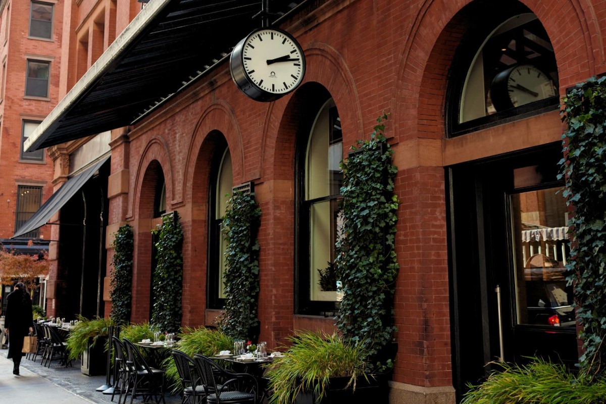 Red brick facade of The Mercer hotel with arched windows, ivy, street clock, and outdoor café tables