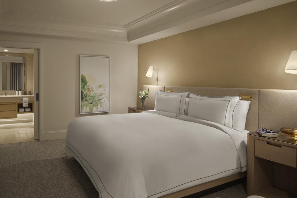 Hotel bedroom with king bed, tan accent wall, bathroom visible through open door
