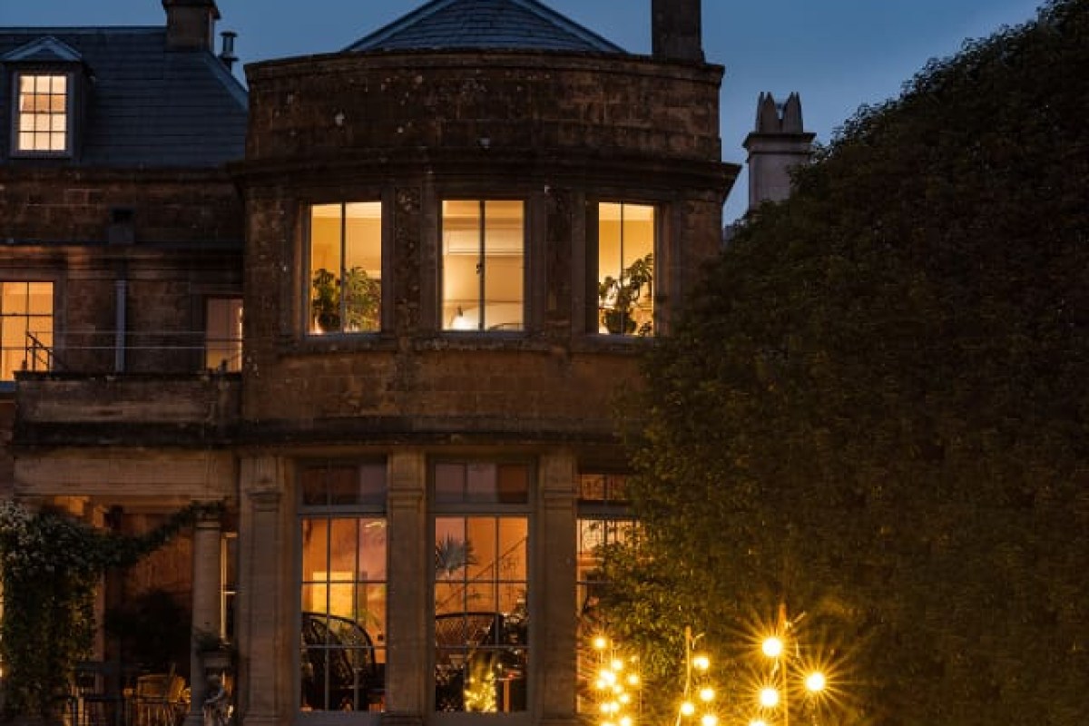 Stone hotel facade at dusk with warm lit windows and soft evening sky