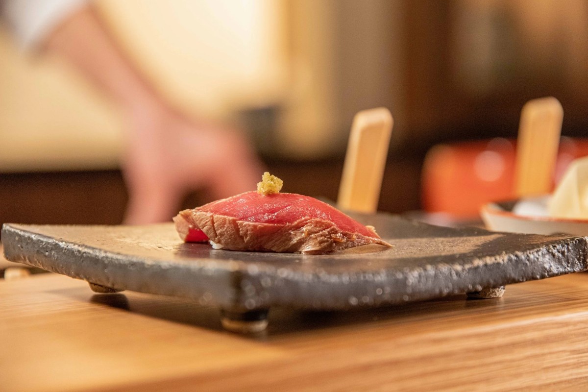 Close-up of a single piece of tuna nigiri sushi on a dark stone plate