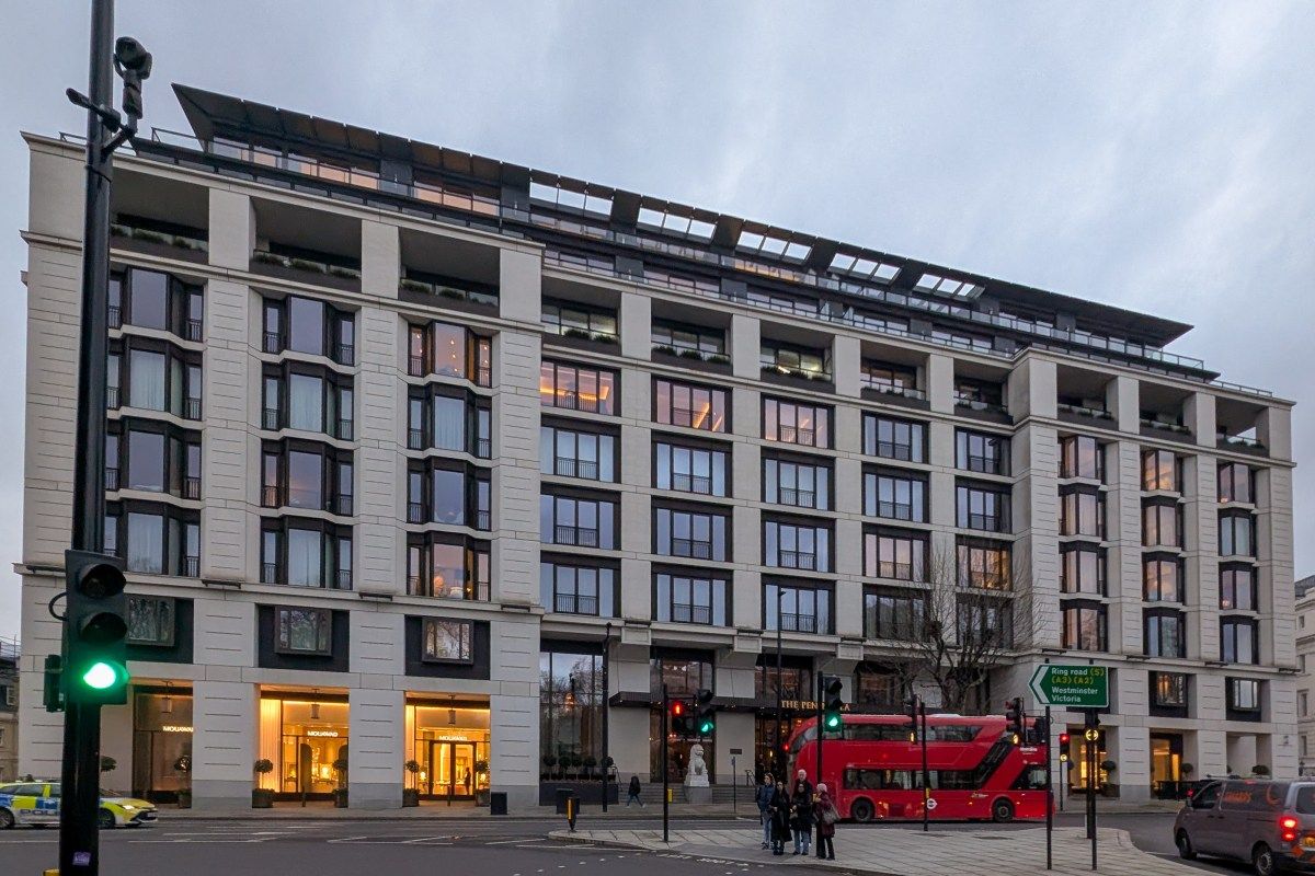 Street-level view of The Peninsula London hotel's cream stone façade at dusk, with red double-decker bus passing
