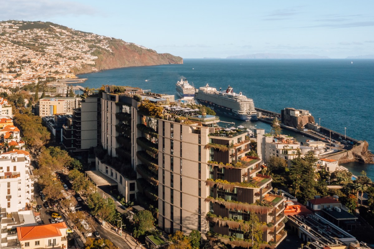 Aerial view of The Reserve Hotel's tiered, plant-covered facade overlooking Funchal bay with cruise ships and coastline.