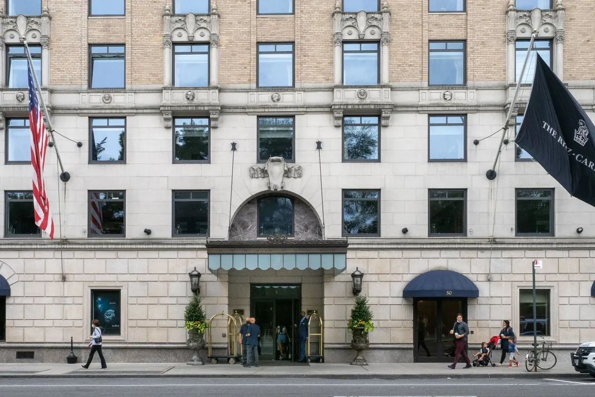 Street-level view of The Ritz-Carlton New York, Central Park entrance with awnings, flags, and bellhop carts