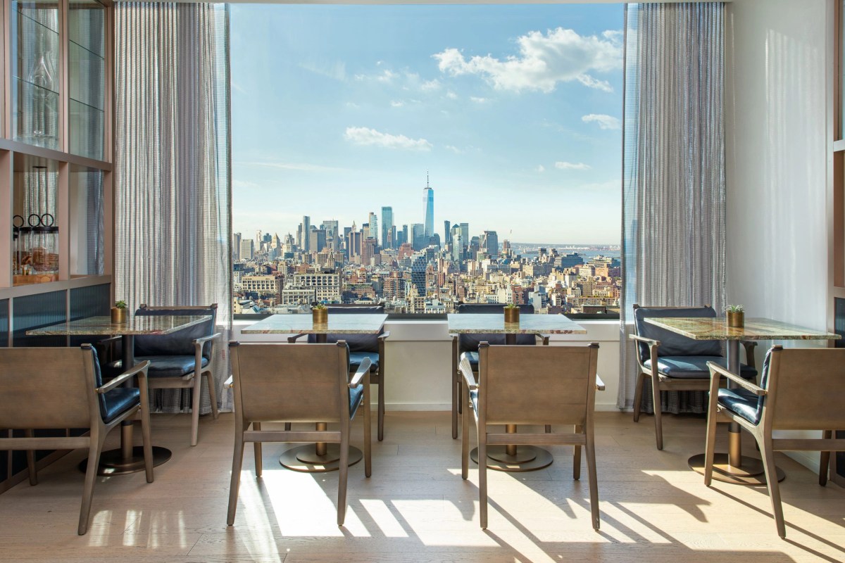 Hotel lounge with tables, chairs and a floor-to-ceiling window overlooking Manhattan skyline