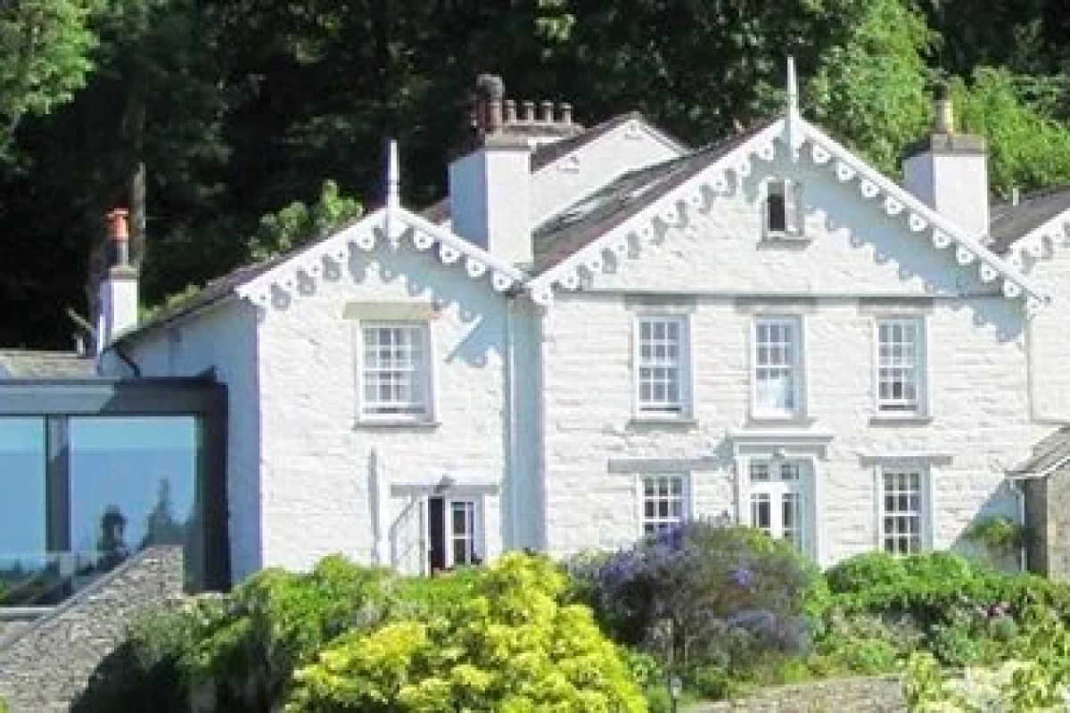 White Lakeland stone building with decorative gable trim, chimneys and windows, surrounded by trees and greenery - the hotel's exterior façade